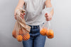 ragazza che porta nelle mani due sacchetti a rete in cotone con frutta